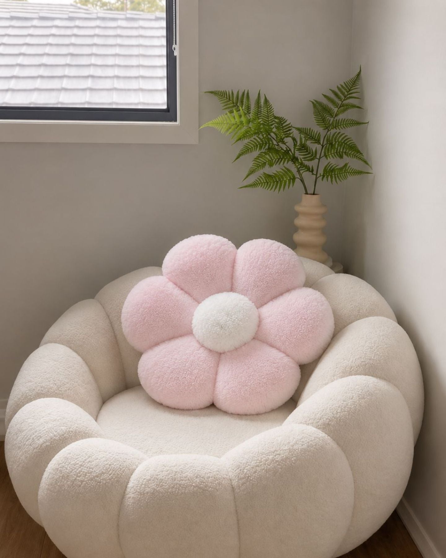 A pink flower-shaped cushion on a cream armchair by a window