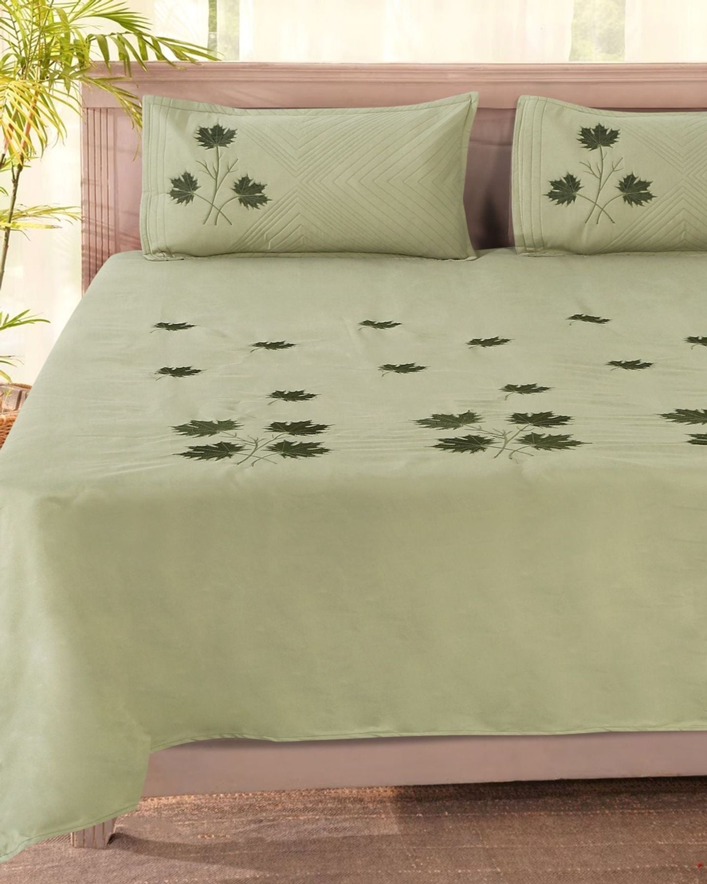 A double bed made with a sage green bedsheet embroidered with dark green leaves